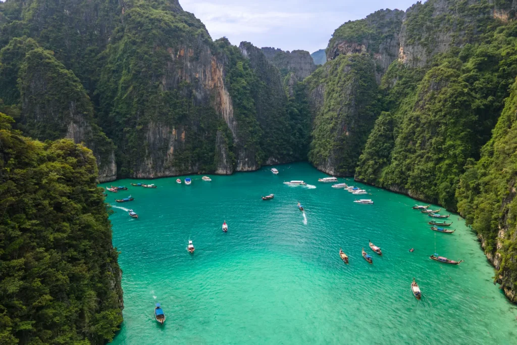 Longtail boats and speedboats in Pileh Lagoon, surrounded by forested limestone cliffs.